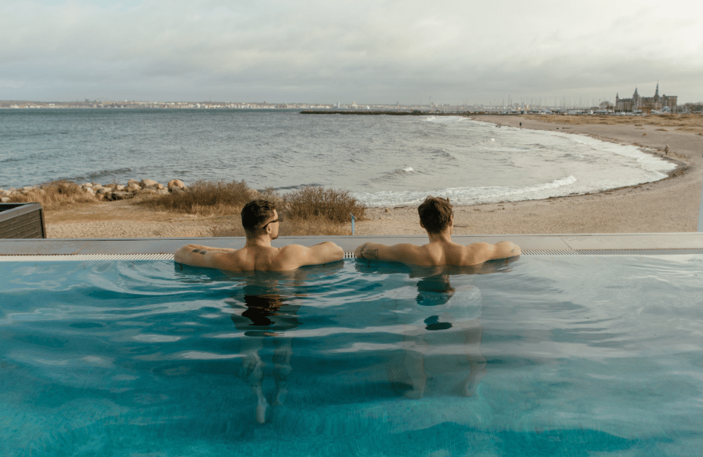 To mænd i en pool kigger ud over Øresund på Marienlyst Badehotel i Nordsjælland